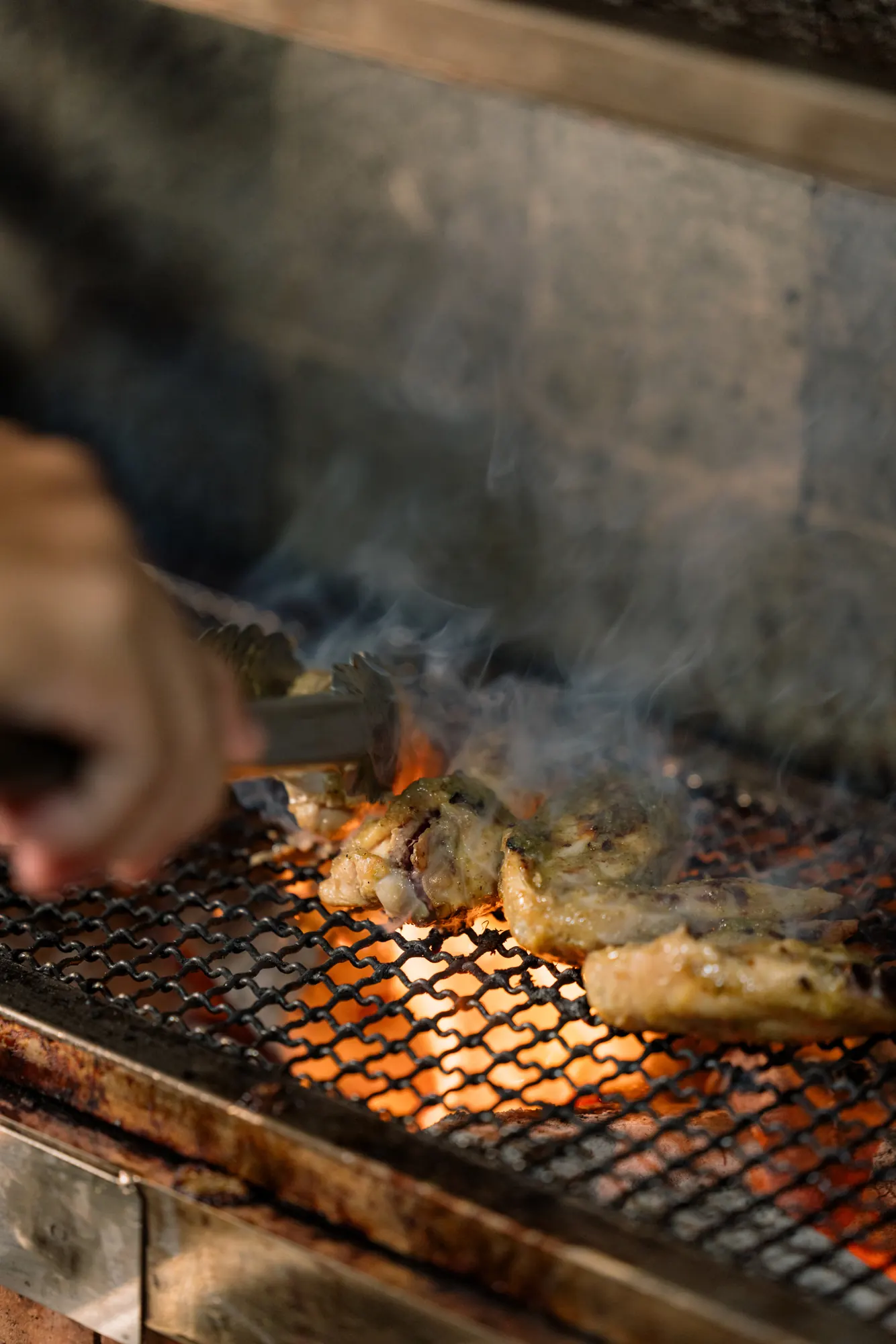 Chicken grilling over charcoal with rising smoke